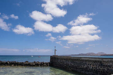 Seascape. Breakwater of the pier of the village of Arrieta with mountains in the background. Turquoise Atlantic Ocean. Big white clouds. Village of Arrieta. Lanzarote, Canary Islands, Spain