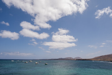Seascape, calm sea. Group of boats anchored nearby. Mountains in the background. Turquoise Atlantic Ocean. Big white clouds. Village of Arrieta. Lanzarote, Canary Islands, Spain