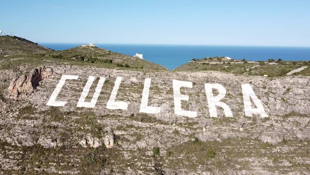 Aerial view approaching the large sign painted on the Sierra de los Zorcos mountain with the name of Cullera, with the Mediterranean Sea in the background, in the province of Valencia (Spain)