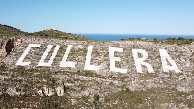 Aerial view approaching the large sign painted on the Sierra de los Zorros mountain with the name of Cullera, with the Mediterranean Sea in the background, in the province of Valencia (Spain)