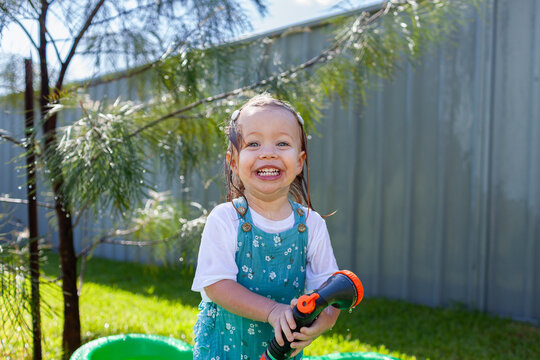 Toddler girl in suburban backyard playing with hose and getting wet in summertime