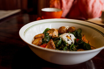 A savory salad with smoked salmon, potatoes, cherry tomatoes, spinach, and a poached egg served in a white bowl.