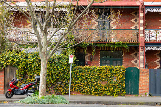 A row of double storey terraces houses on a city street with intricate brickwork and ivy
