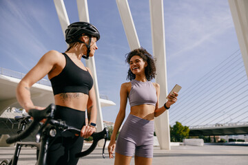 Two sporty female friends talking while standing in city before training