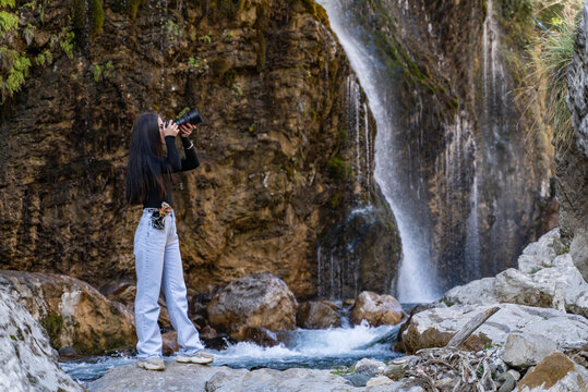beautiful girl taking a photo in front of the waterfall.