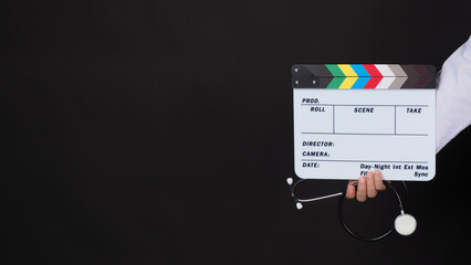 Doctor's hand holding stethoscope and clapper board on black background.