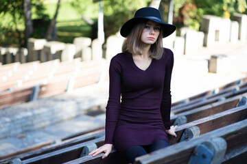 A lonely girl in a black hat sits in on a summer theater bench