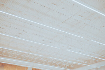Long shop LED lights hanging over modern suspended ceiling metal roof structure, warehouse industry...