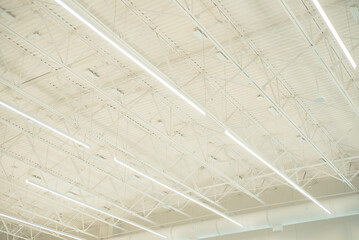 Long shop LED lights hanging over modern suspended ceiling metal roof structure, warehouse industry factory building lighting solution background, perimeter track membrane truss, Frisco, TX - obrazy, fototapety, plakaty