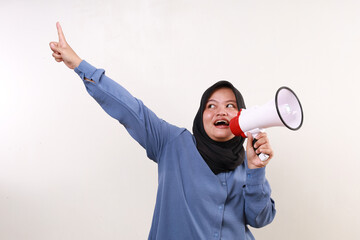 Joyful asian adult muslim woman pointing above while shouting using megaphone
