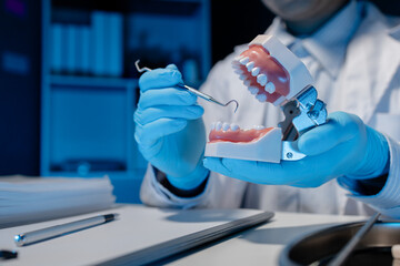 An oral surgeon is using a specialized dental instrument to inspect the mouth of a denture as he practices treating a patient, Denture is being examined by dentists for use in practicing their skills.