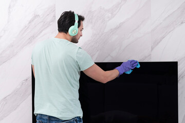 Back view of young man wiping television with a rag and spray	
