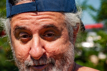 Face portrait of old senior bearded Hispanic man with sly look, closeup