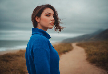 A woman wearing a blue jacket stands on a dirt road. - Powered by Adobe