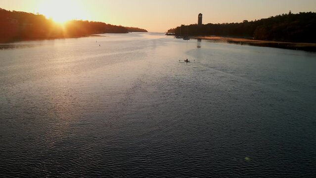 Cinematic drone shot of a woman taking off solo paddling on calm water with a beautiful sunrise in an ocean bay in Halifax, Canada. Solo rower 