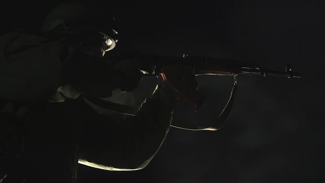 AMBIENT SOUND. Silhouette of warfare soldier in dark with combat ammunition and weapons in hands, machine gun fires bursts towards the enemy. Infantryman shoots from a machine gun. Cinematic video