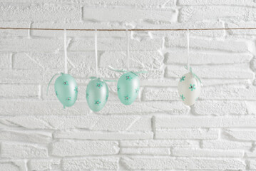 Turquoise Easter eggs hanging on a rope against a white brick wall. - 759754309