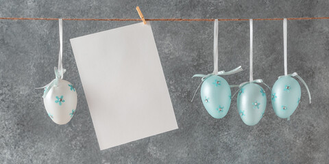 Blue Easter eggs and a blank white card mockup hanging on a rope, gray concrete background. Banner - 759755596