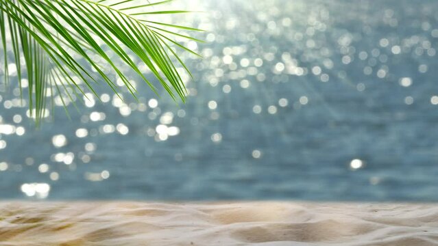 fresh green palm leaf and white sand on blurred glittering bokeh light water background, beautiful idyllic sand beach backdrop with product display for summer vacation, travel and relaxation outdoors