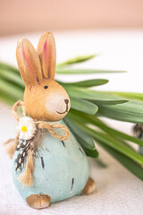 Cute ceramic rabbit and green leaves in the background. Eastern, spring decorative crafts, DIY concept
