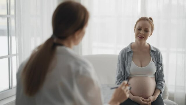 Pregnant woman consulting with a doctor. Smiling pregnant woman patient answers gynecologist questions at hospital, medical clinic. Doctor examine pregnant belly check up. Gynecology concept.