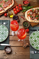Two glasses of Aperol spritz cocktail on wooden table, served with tableware and pizza