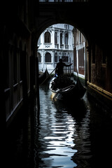 gondolier navigating a gondola through a shadowy Venetian canal, with light illuminating the intricate architecture of surrounding buildings. - obrazy, fototapety, plakaty