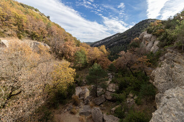 A scenic view of a forested valley with autumn foliage, rocky terrain, and a clear sky in boltaña