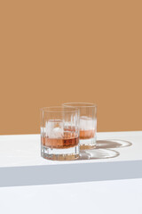 Dos vasos de whisky con hielo sobre un fondo naranja