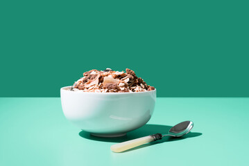 Cereal de granola muesli en un tazón blanco con cuchara sobre fondo verde	
