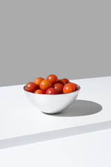Tomates cherry maduros en un bol plateado sobre fondo gris