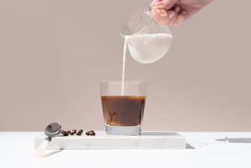 Vertiendo leche en un vaso trasparente de café sobre mármol y fondo beige
