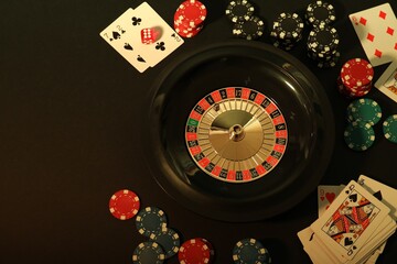 Roulette wheel, playing cards and chips on table, flat lay with space for text. Casino game