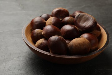Roasted edible sweet chestnuts in bowl on grey table, closeup