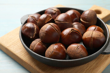 Fresh edible sweet chestnuts in frying pan on light blue wooden table, closeup