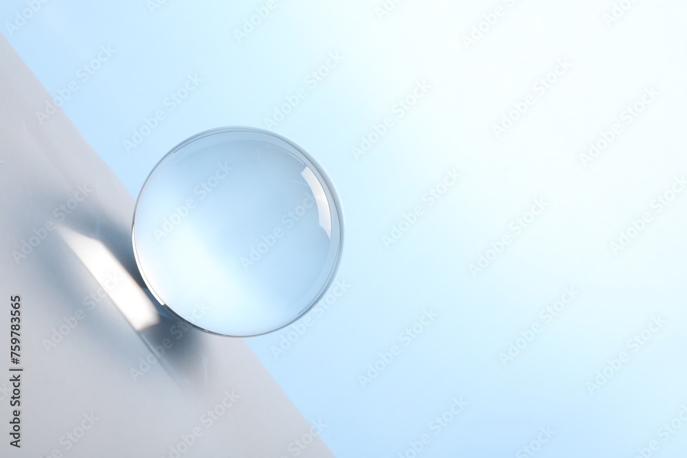 Wall mural Transparent glass ball on table against light blue background. Space for text