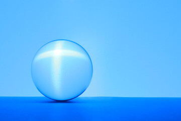 Transparent glass ball on table against light blue background. Space for text