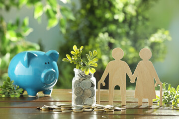 Pension savings. Figure of senior couple, piggy bank, coins and green twigs on wooden table outdoors