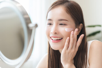 Facial beauty skin health care, smile of cute asian young woman looking at mirror, hand applying...