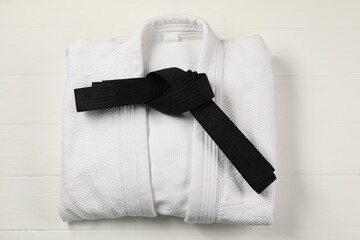 Black karate belt and white kimono on wooden background, top view