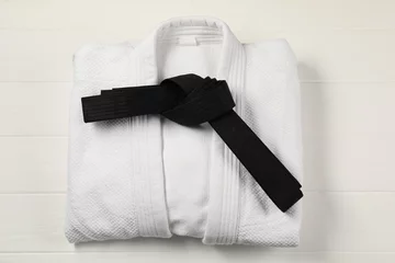 Tuinposter Black karate belt and white kimono on wooden background, top view © New Africa