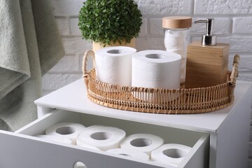 Toilet paper rolls, floral decor, dispenser and cotton pads on chest of drawers indoors