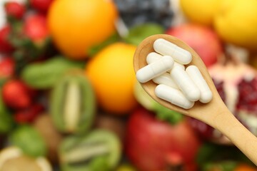 Vitamin pills in spoon over fresh fruits, top view. Space for text