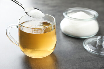 Adding sugar into aromatic tea at grey table, closeup
