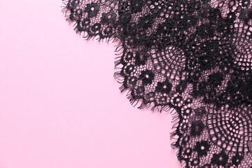 Black lace on pink background, top view. Space for text