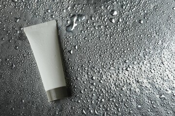 Moisturizing cream in tube on silver background with water drops, top view. Space for text