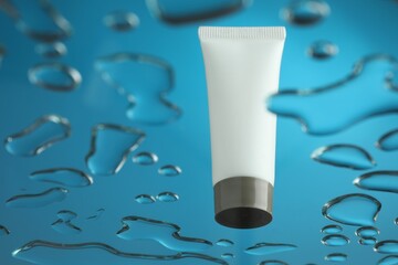 Moisturizing cream in tube on glass with water drops against blue background, low angle view. Space for text
