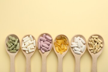 Different vitamin pills in spoons on pale yellow background, flat lay. Space for text