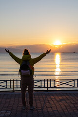 Silhouette of a person with arms raised, greeting the sunrise by the sea. - 759792981