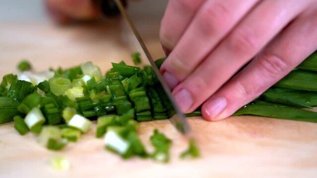 Woman cutting greens on wooden board outdoors. Close up of woman's hands cutting verdure with knife on chopping board. Unrecognizable lady cutting greens on wooden board outdoors. Woman's hands with